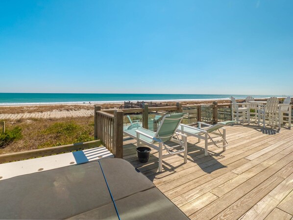 Une terrasse en bois avec des chaises longues et une table, donnant sur une plage.