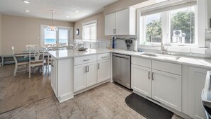 A modern kitchen with white cabinetry, a large island, and a view of the ocean. - Beach Coma | Oceanfront, Hot Tub on the Deck! (Topsail Beach)