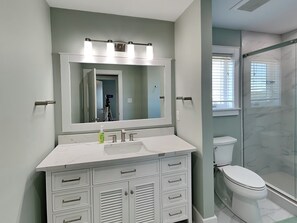 A bathroom with a large mirror, a sink, a toilet, and a shower area. - Beach Coma | Oceanfront, Hot Tub on the Deck! (Topsail Beach)