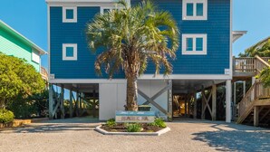 A two-story building with a blue exterior and white trim, featuring a palm tree in the center. - Beach Coma | Oceanfront, Hot Tub on the Deck! (Topsail Beach)