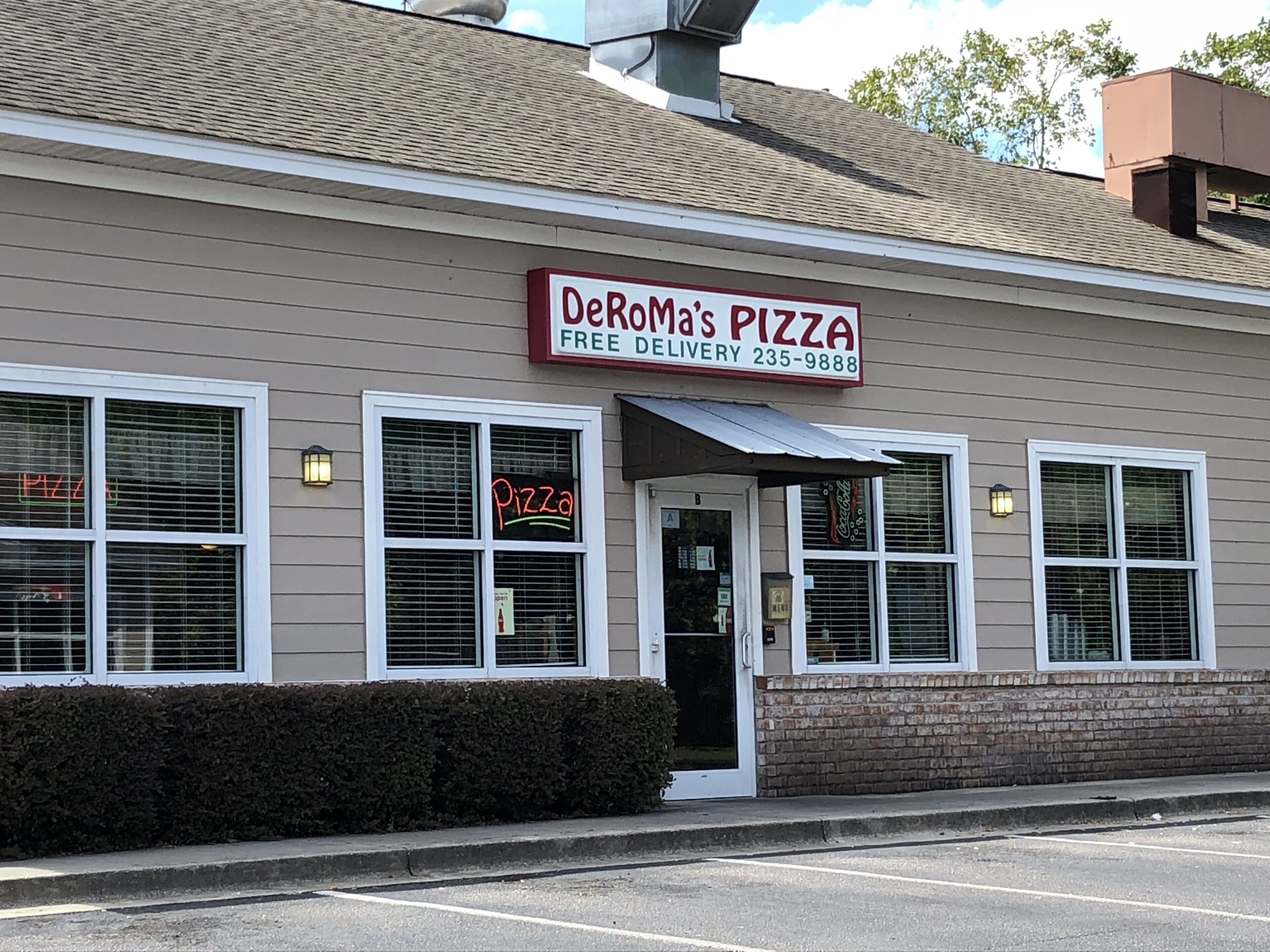 A building with a sign reading "DeRoMa's Pizza" and a neon sign above the door.