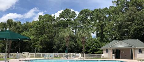 Un área de piscina con sillones de descanso, un edificio pequeño y una cerca blanca.