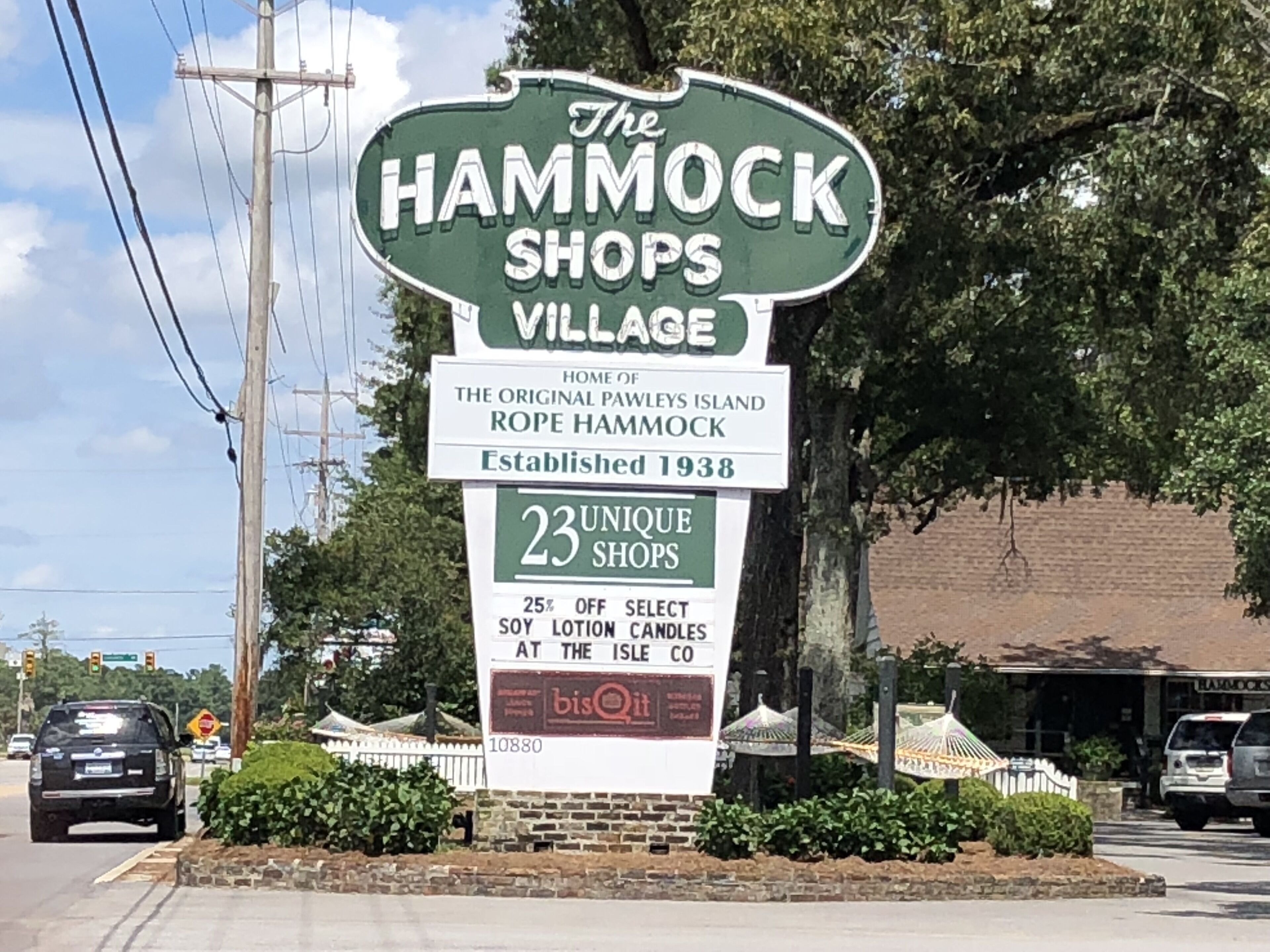 A sign for The Hammock Shops Village, indicating it is home of the original Pawleys Island Rope Hammock, established in 1938, with 23 unique shops and a 25% off offer on select items.