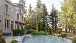 Una piscina rodeada por un jardín, con una casa al fondo.