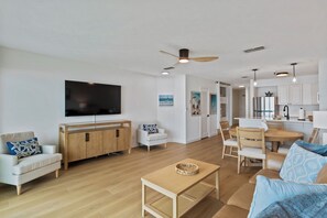 A modern living room with a flat-screen TV, wooden furniture, and a dining area.