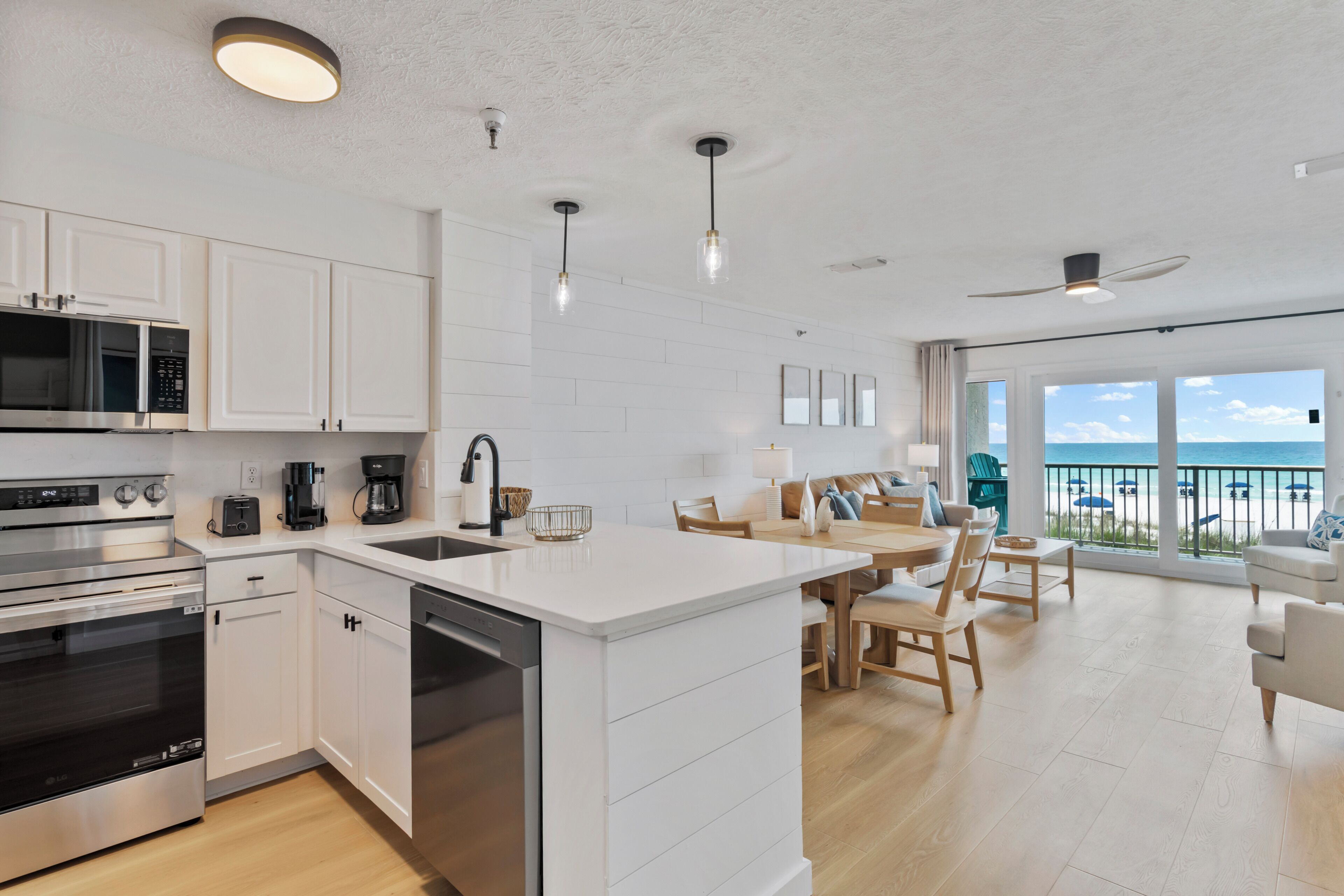 A modern kitchen with stainless steel appliances, a white island, and a dining area with wooden furniture.