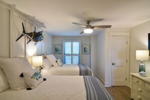 Two single beds with white bedding and decorative pillows, a ceiling fan, and a window with blinds.