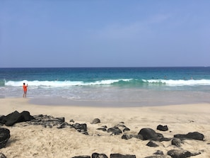 A beach with clear skies, waves, and a person in red.