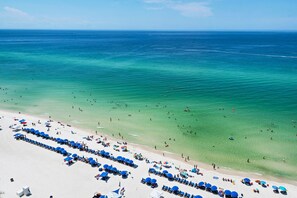 A beach with rows of blue umbrellas and sun loungers, clear turquoise water, and a sandy shore.