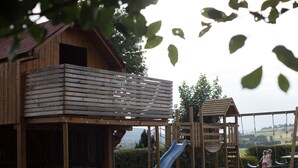 A wooden play structure with a slide and climbing elements, set in a grassy area with a view of the countryside. - Gästehaus Weber (Arrach)
