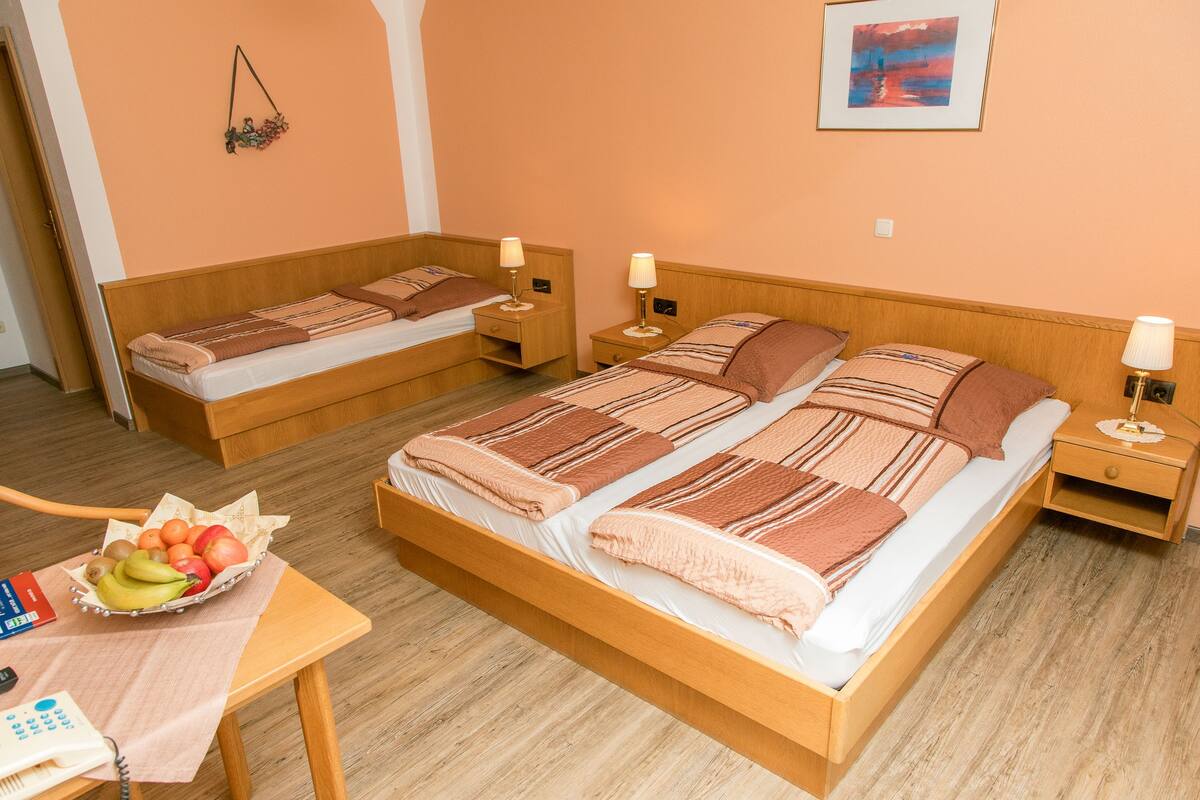Habitación de hotel con dos camas, cabeceros de madera, mesitas de noche con lámparas, una cesta de frutas y un escritorio con teléfono.
