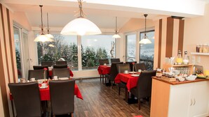 A dining area with tables set for breakfast, large windows with a view of snow-covered trees, and a buffet counter with food items. - Gästehaus Weber (Arrach)