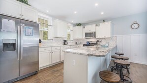 A modern kitchen with white cabinets, stainless steel appliances, a marble countertop, and wooden stools. - Hot tub, EV friendly, main floor primary suite with plenty of space. (South Haven)