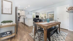 A modern kitchen with white cabinets, a stainless steel refrigerator, and a dining area with a wooden table and metal chairs. - Hot tub, EV friendly, main floor primary suite with plenty of space. (South Haven)