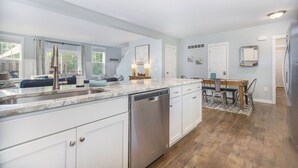 A modern kitchen with white cabinetry, a dishwasher, and a dining area with a wooden table and chairs. - Hot tub, EV friendly, main floor primary suite with plenty of space. (South Haven)
