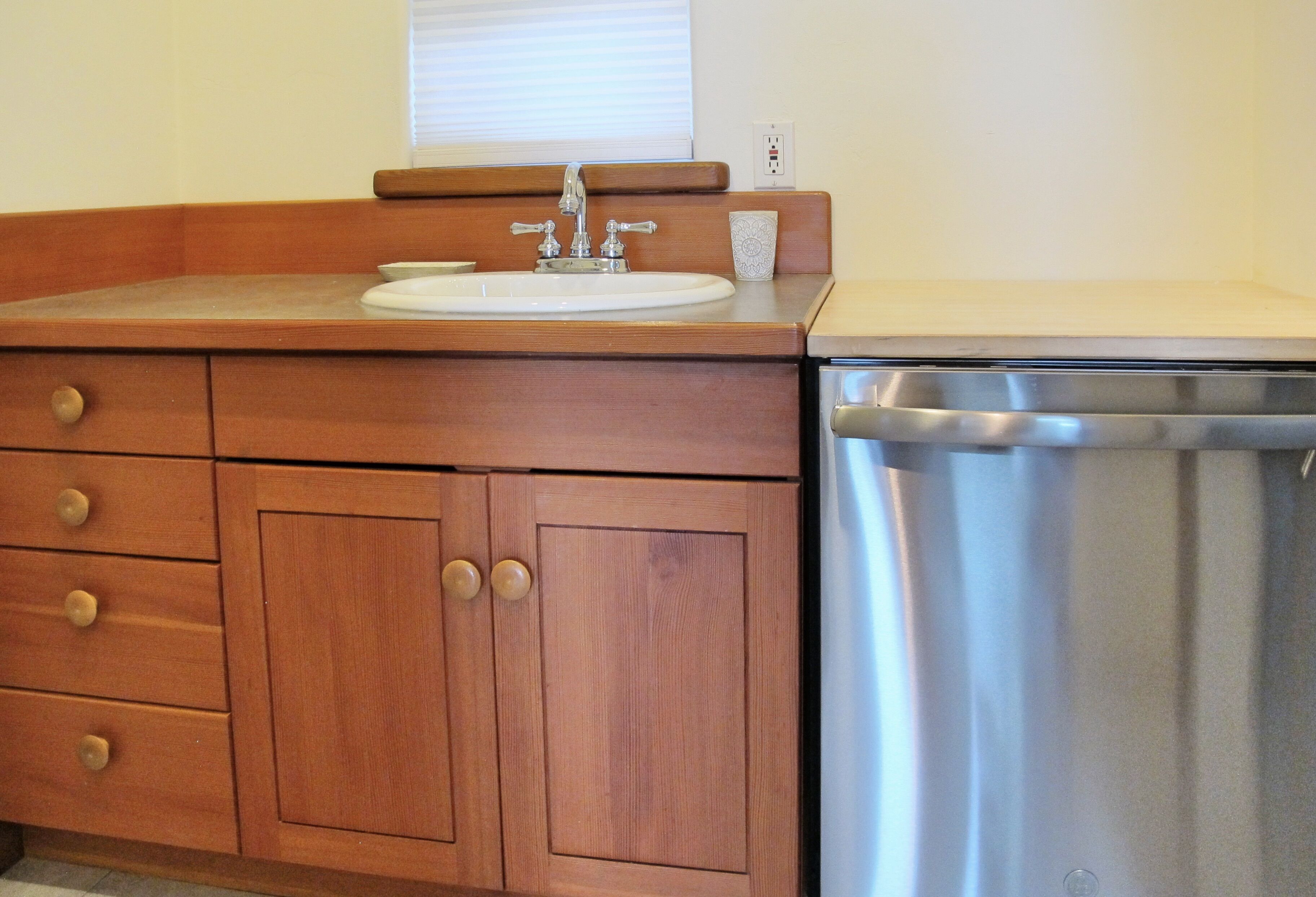 A wooden vanity with a sink, a mirror, and a stainless steel dishwasher.