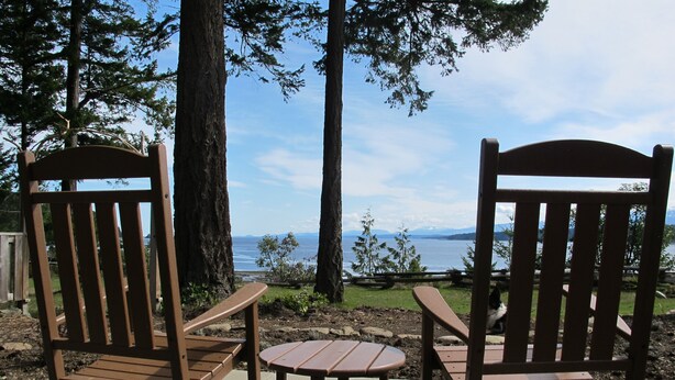 Two wooden Adirondack chairs facing a lake with mountains in the distance. - Beautiful Oceanfront ‘Cottage’ - Breathtaking Views,Beach,Pet Friendly,Fireplace (Denman Island)