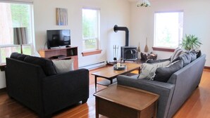 A living room with a sofa, a coffee table, a TV, and a fireplace. - Beautiful Oceanfront ‘Cottage’ - Breathtaking Views,Beach,Pet Friendly,Fireplace (Denman Island)