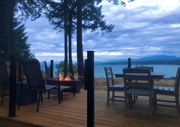 Relax by the fire pit on the deck, surrounded by comfortable seating and a serene view of the water and mountains.