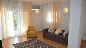 A living room with a sofa, armchair, patterned rug, and curtains.
