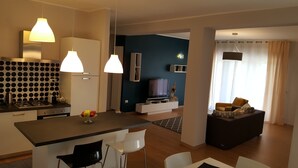 A modern living space with a kitchen, dining area, and a seating area with a sofa and a TV.