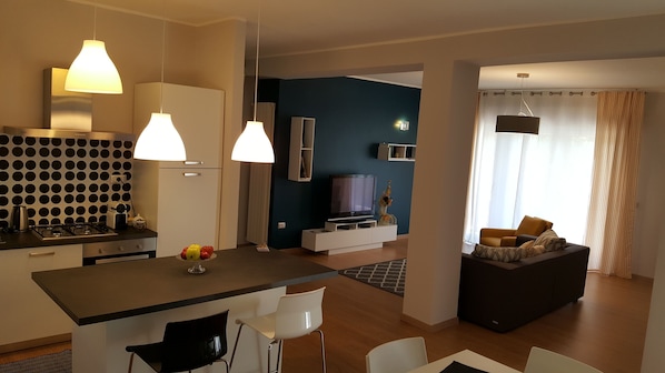 A modern living space with a kitchen, dining area, and a seating area with a sofa and a TV.