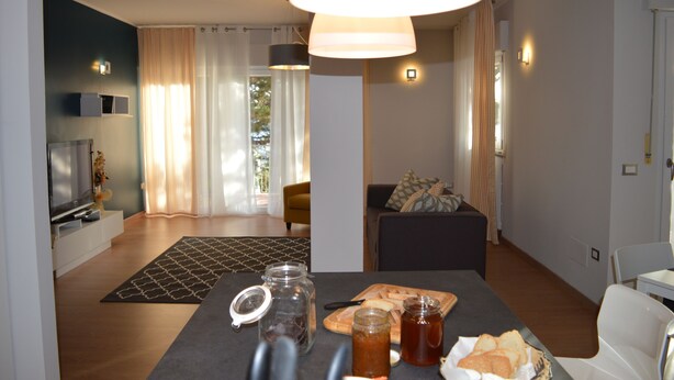 A modern living room with a flat-screen TV, a dining area with a table set for two, and a sofa.