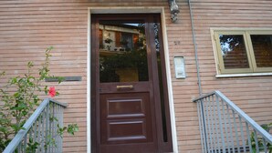 A brown door with a handle, a small window with a light fixture above it, and a metal railing to the right.