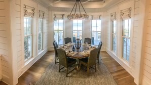Une salle à manger avec une table ronde dressée pour six personnes, entourée de chaises, et un lustre au-dessus.