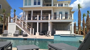 Une maison à deux étages avec une piscine, un espace salon extérieur et des palmiers.