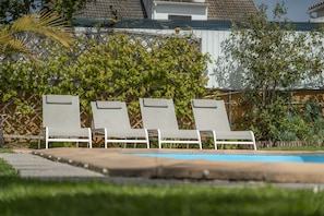 A pool area with three lounge chairs and a wooden deck.