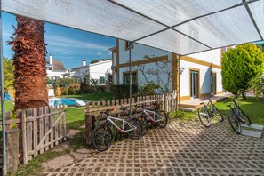 Et overdækket udendørsområde med cykler, et træhegn og et hus i baggrunden.