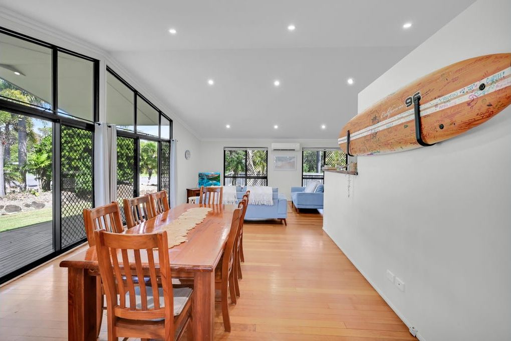 A spacious dining area with a long wooden table and chairs, a blue sofa, and a surfboard mounted on the wall.
