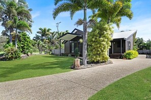 A modern house with a covered outdoor area, surrounded by lush greenery and palm trees.