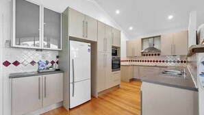 A modern kitchen with light-colored cabinets, a refrigerator, oven, and a microwave. - Gathering of 8 Holiday House (Agnes Water)