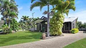 A modern house with a covered outdoor area, surrounded by lush greenery and palm trees. - Gathering of 8 Holiday House (Agnes Water)