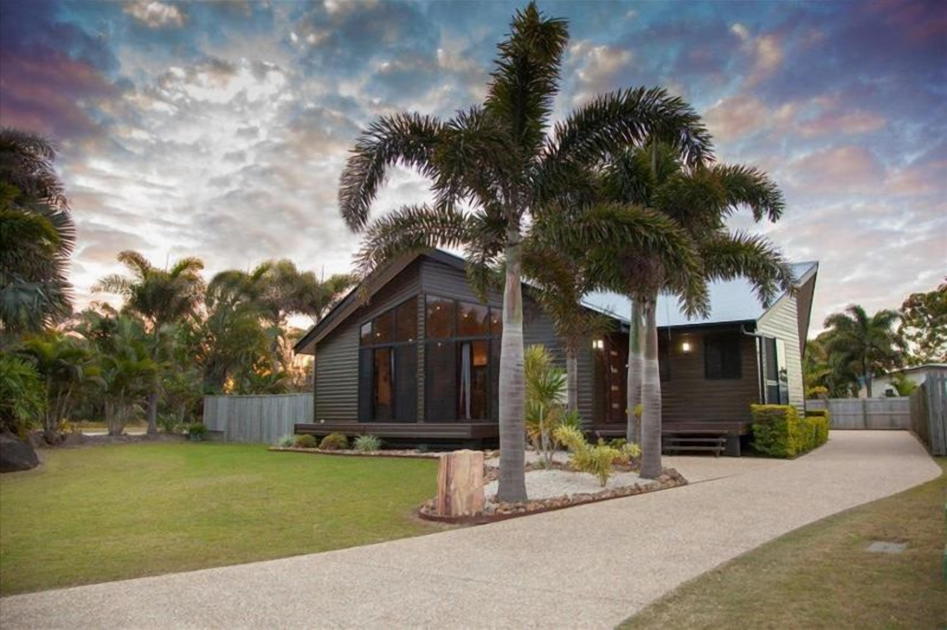 A modern two-story house with a large front yard, palm trees, and a well-maintained lawn.