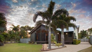A modern two-story house with a large front yard, palm trees, and a well-maintained lawn. - Gathering of 8 Holiday House (Agnes Water)