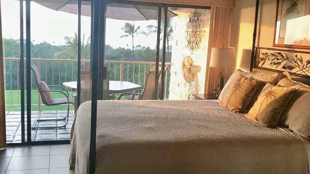 Une chambre avec un grand lit, un balcon avec une table et des chaises, et une vue sur les palmiers.