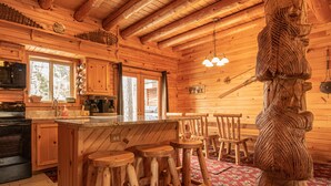 Innenansicht einer Holzhütte mit Küche, Bar und einer ungewöhnlichen Holzskulptur.