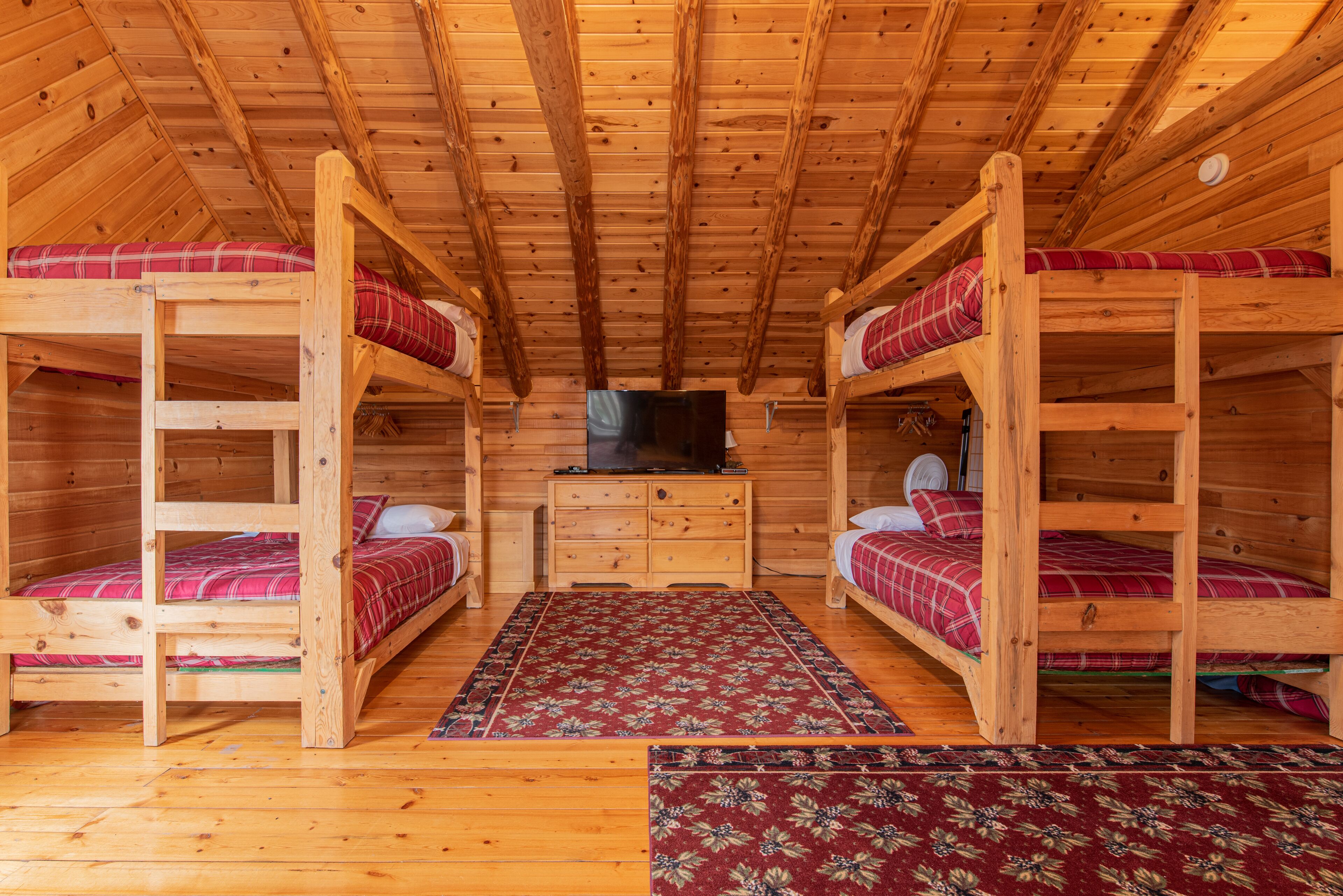 Une cabane en bois avec des lits superposés, une commode centrale et un téléviseur.