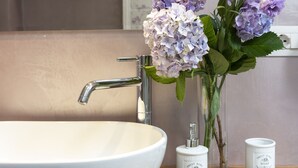A bathroom with a white sink, a mirror, and a vase with purple flowers. There are two bottles of soap on a tray. - The Gelda house, relax with a view (Castelnuovo dell'Abate)