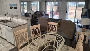 A modern living room with a kitchen area, a dining table with chairs, a sofa, and a television.