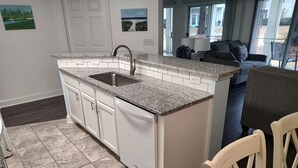 A kitchen with white cabinets, granite countertops, and a sink. There is a dining area with a table and chairs.