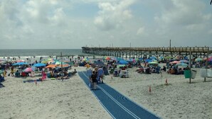 A beach with a pier, umbrellas, and people.