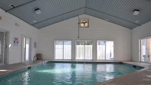 An indoor swimming pool with a high ceiling, large windows, and a clear view of the outside.