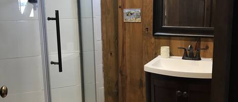 A bathroom with a glass-enclosed shower, wooden paneling, a white sink, and a mirror above it.