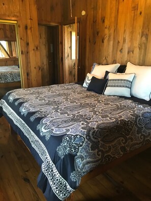 A wooden room with a bed featuring a patterned bedspread and pillows. - Cozy Creek Front Retreat (Pawleys Island)
