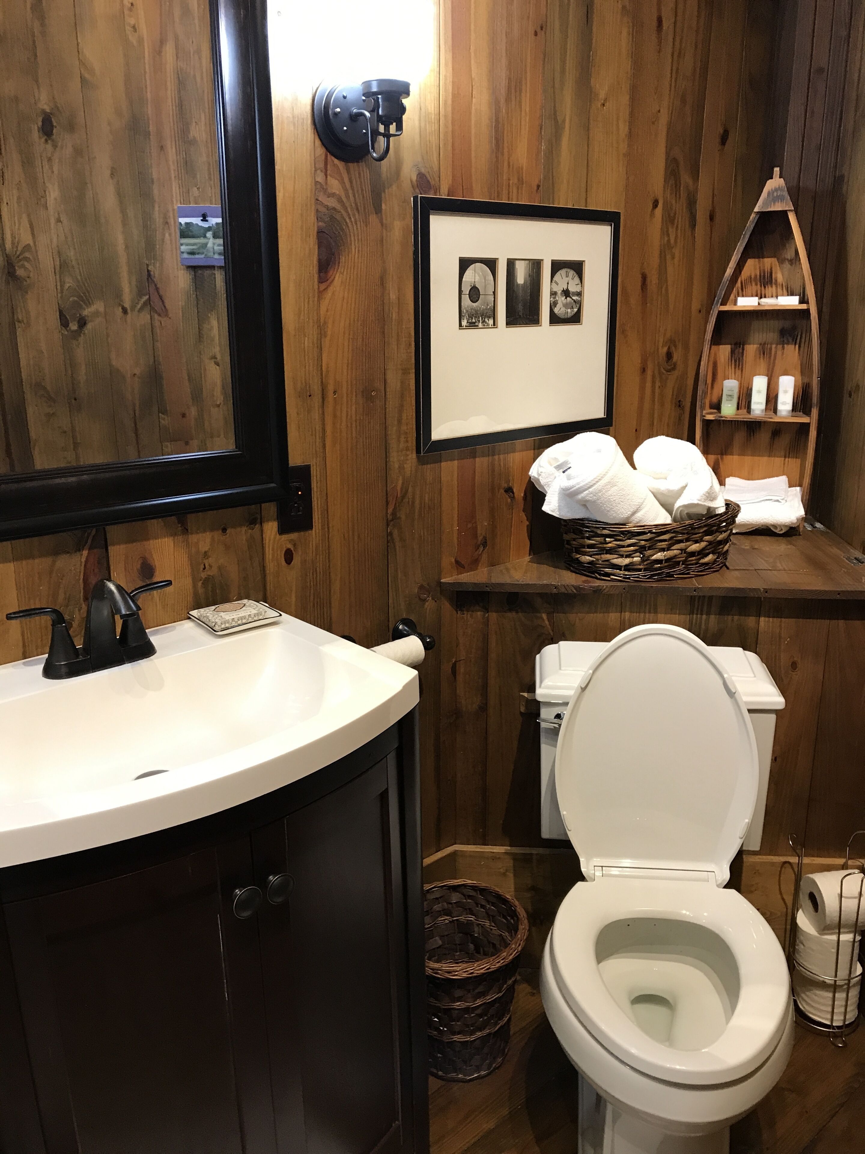 Une salle de bain en bois avec un lavabo blanc, des toilettes et une photo encadrée au-dessus du lavabo.