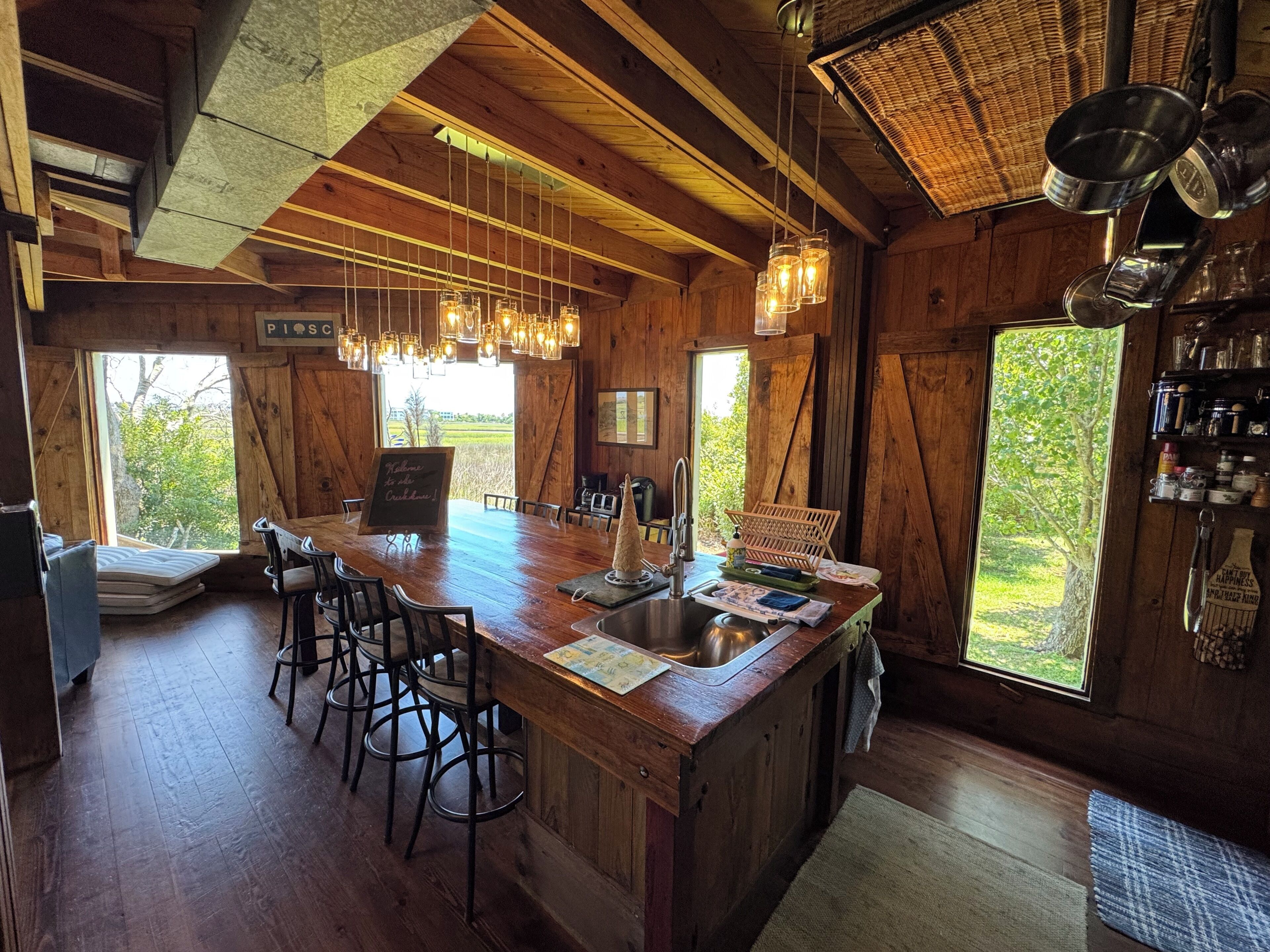 Un intérieur en bois avec un îlot central, des tabourets de bar, des luminaires suspendus et une vue dégagée grâce à de grandes fenêtres.